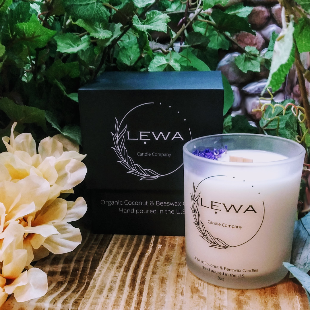 'Confidence' Candle in a frosted glass jar with dried floral decoration, next to the signature LEWA black logo box, set against a faux stone wall with faux floral.