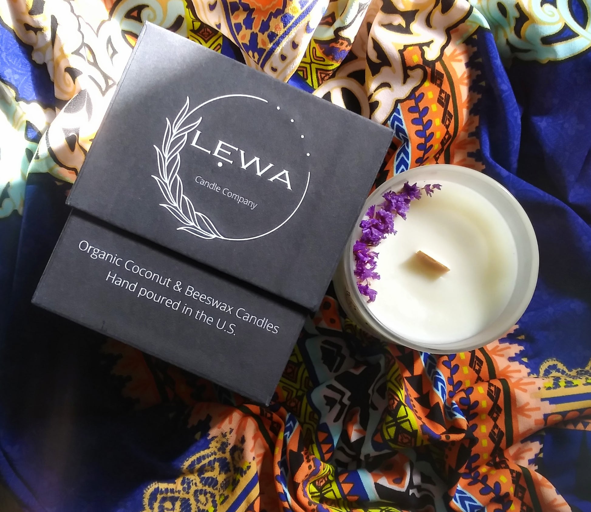 Top view of 'Confidence' Candle with dried floral decoration on top, beside the LEWA black signature box on patterned fabric.